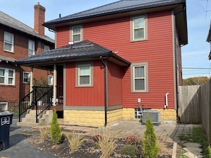 A two-story red house with a covered porch and a small garden.