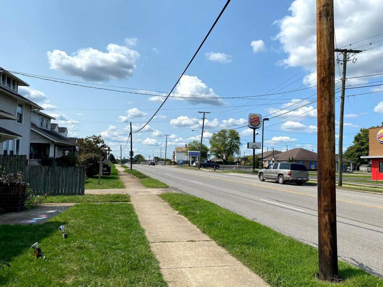 A suburban street with a sidewalk, houses, a road, and a Burger King sign.