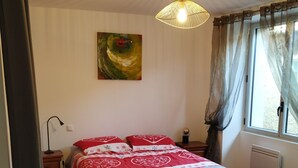 Une chambre à coucher avec un lit, un luminaire suspendu, un radiateur et une fenêtre avec des rideaux.