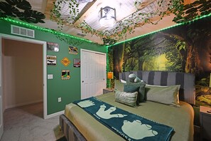 Een slaapkamer met een groene wand, een bed met een groen-witte deken, een nachtkastje met een lamp en een muurschildering van een bos.