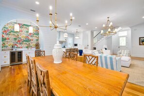 A spacious living area with a wooden dining table, white sofas, and a kitchen in the background. - Beautiful Beach Home Near Seaside with Pool, LSV, Firepit and Pool Table (Santa Rosa Beach)