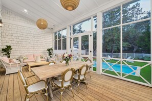 A covered patio with a wooden table and wicker chairs, overlooking a swimming pool and a white picket fence. - Beautiful Beach Home Near Seaside with Pool, LSV, Firepit and Pool Table (Santa Rosa Beach)