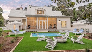 Una casa de dos pisos con un amplio porche delantero, piscina y mobiliario de exterior.