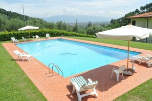 Relax by the pool surrounded by lush greenery and distant hills.