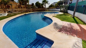 A swimming pool with a curved design, surrounded by a stone wall and a wooden fence. - Paraíso Benahavís - Private Garden Ground Floor (Benahavís)