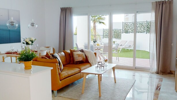 A modern living room with a sofa, coffee table, and dining area. There is a sliding glass door leading to an outdoor patio with a table and chairs. - Paraíso Benahavís - Private Garden Ground Floor (Benahavís)