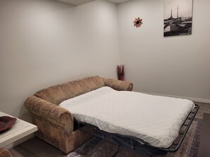 Quarto com uma cama de solteiro, um sofá marrom, uma mesinha e um quadro na parede.