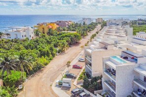 A coastal residential area with modern buildings, a road, and parked cars.