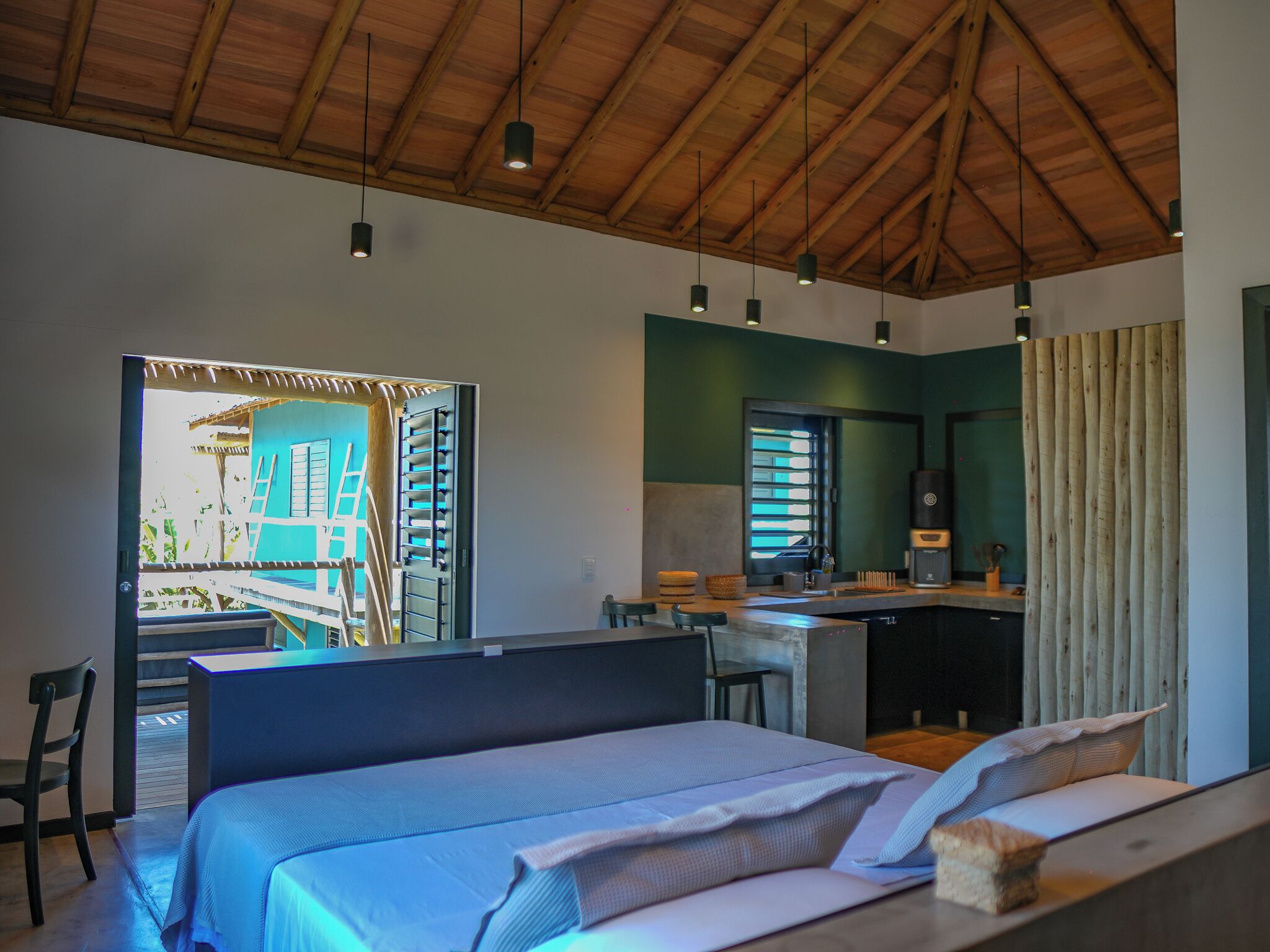A modern bedroom with a bed, a desk, and a kitchenette.