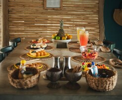 A wooden table with various food items and drinks, including a pineapple, fruits, and a glass of juice.