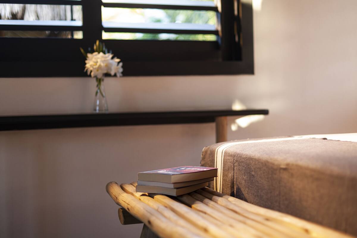 A wooden bench with a stack of books and a vase with flowers on a windowsill.
