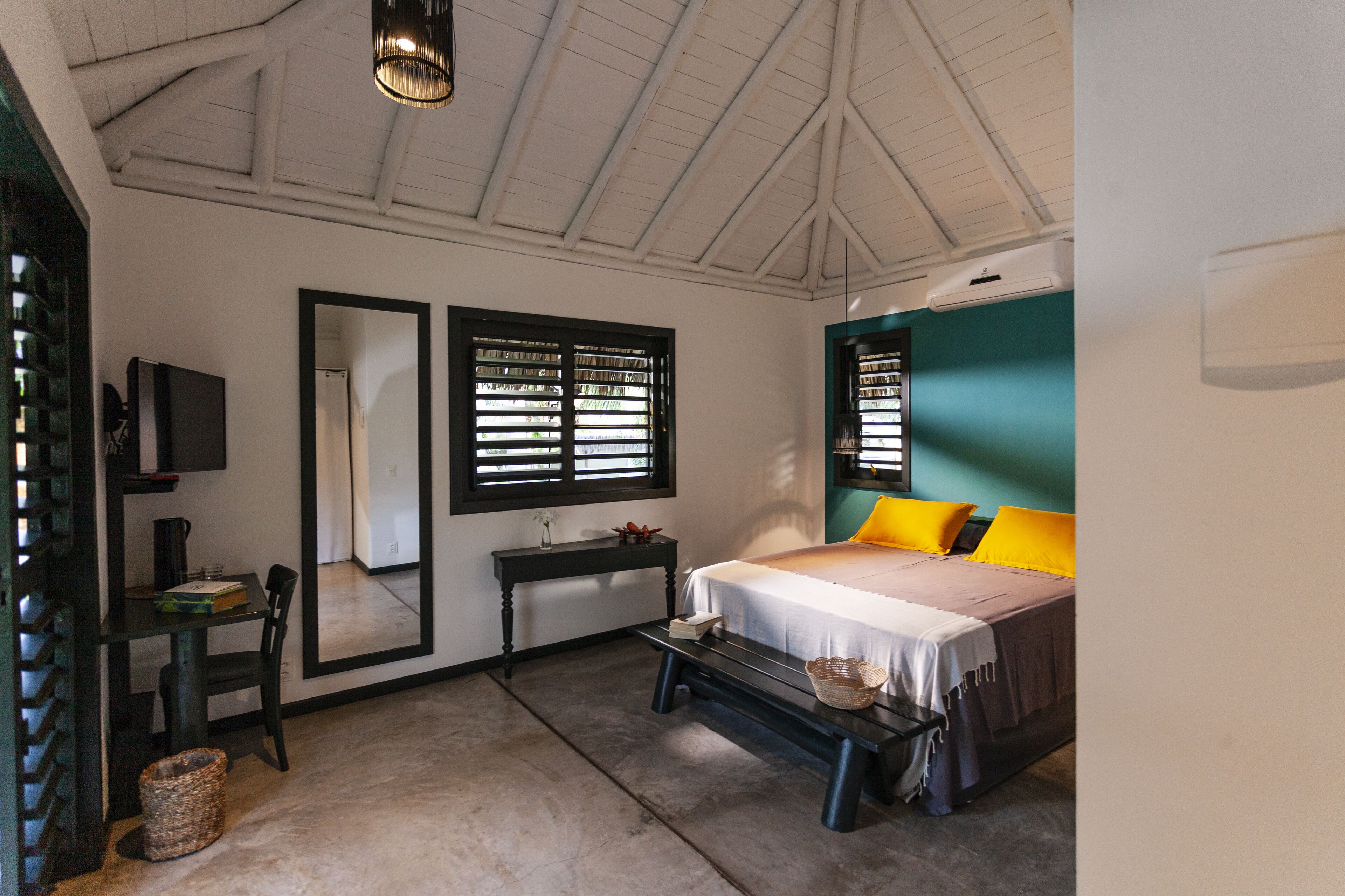 A bedroom with a bed, a desk, a chair, a TV, and a window with blinds.