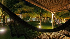 A hammock under a wooden pergola with palm trees and a well-lit outdoor area. - Hotel VilaVeraTheresa  (Fortim)