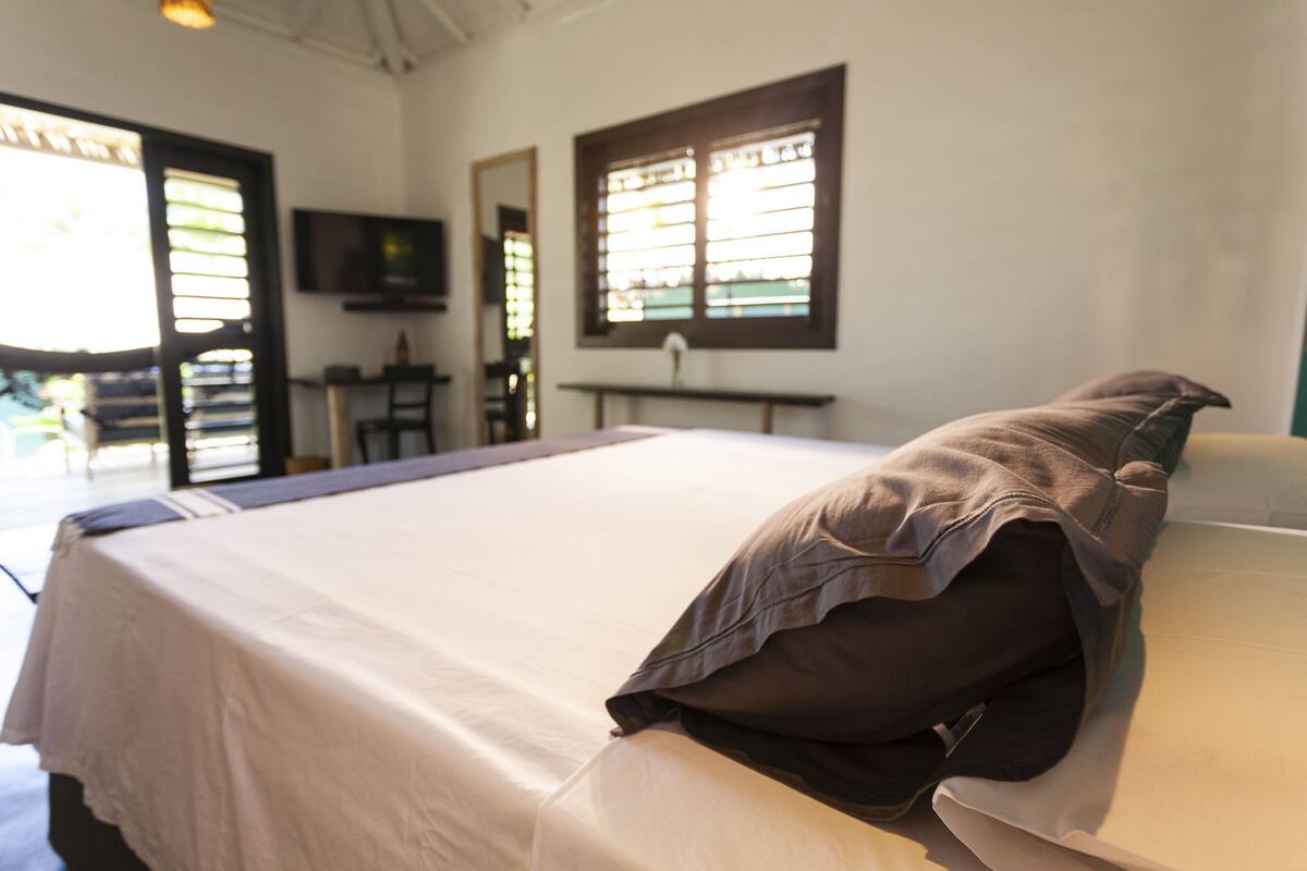 A neatly made bed with a pillow and a bedside table in a room with a television and a window.