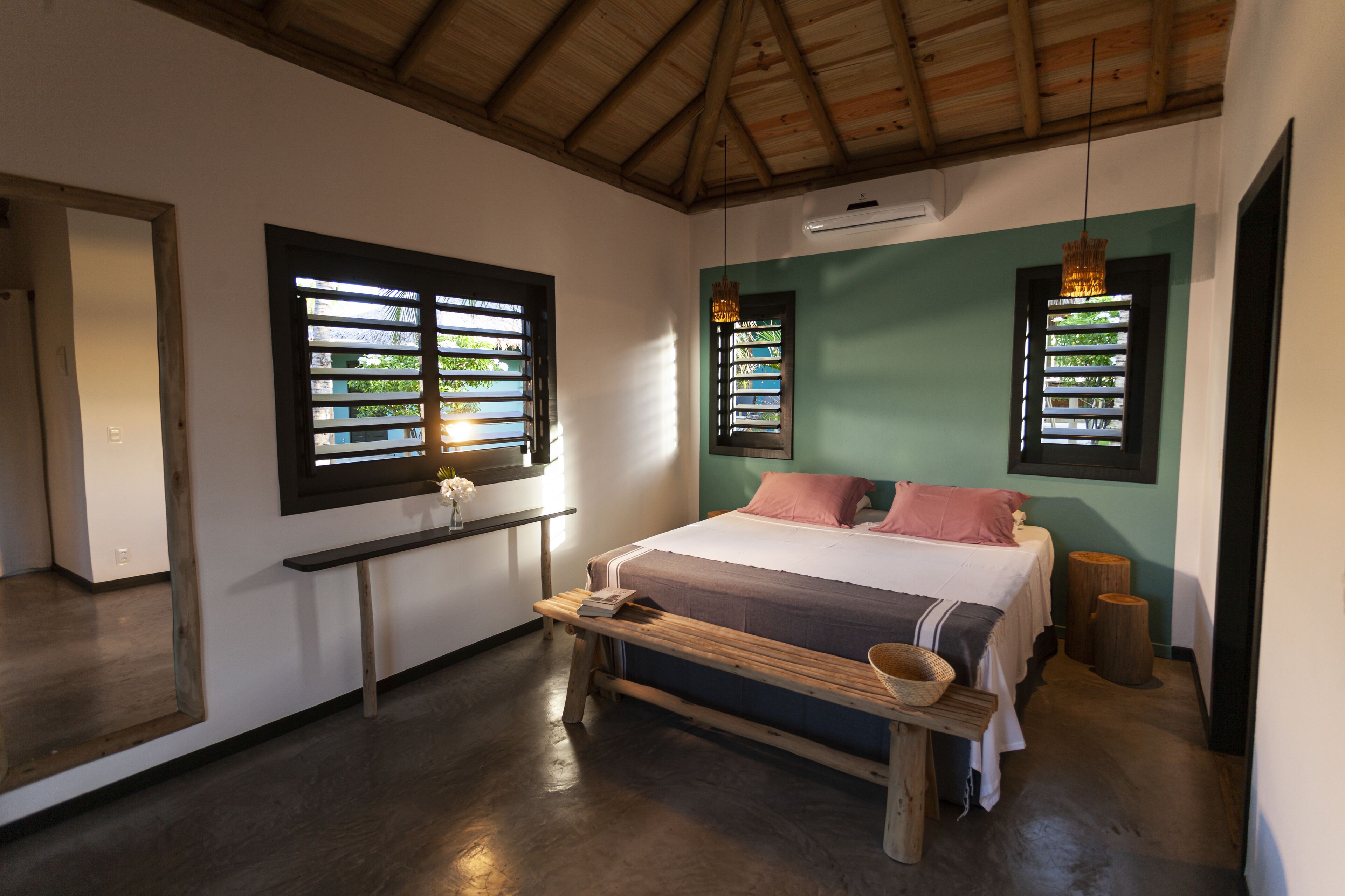 A bedroom with a bed, a bench, and two windows with blinds.