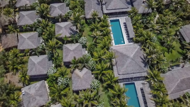 An aerial view of a resort with thatched-roof cottages arranged in rows, surrounded by lush greenery and featuring central swimming pools. - Hotel VilaVeraTheresa  (Fortim)