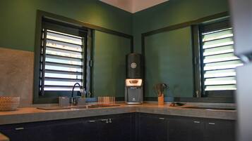 A kitchen with a coffee maker, a sink, and a window with blinds.