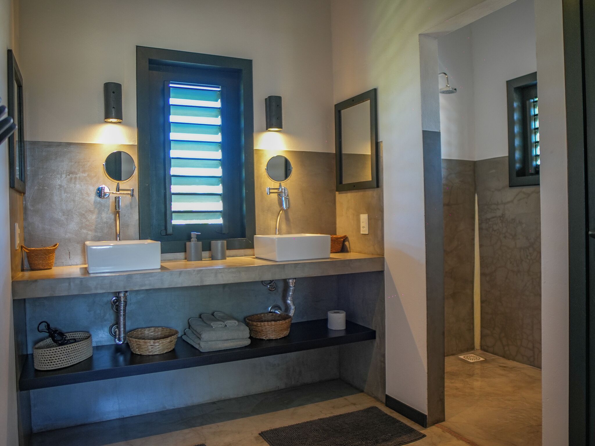 A modern bathroom with two sinks, a window with blinds, a mirror, and a towel rack.
