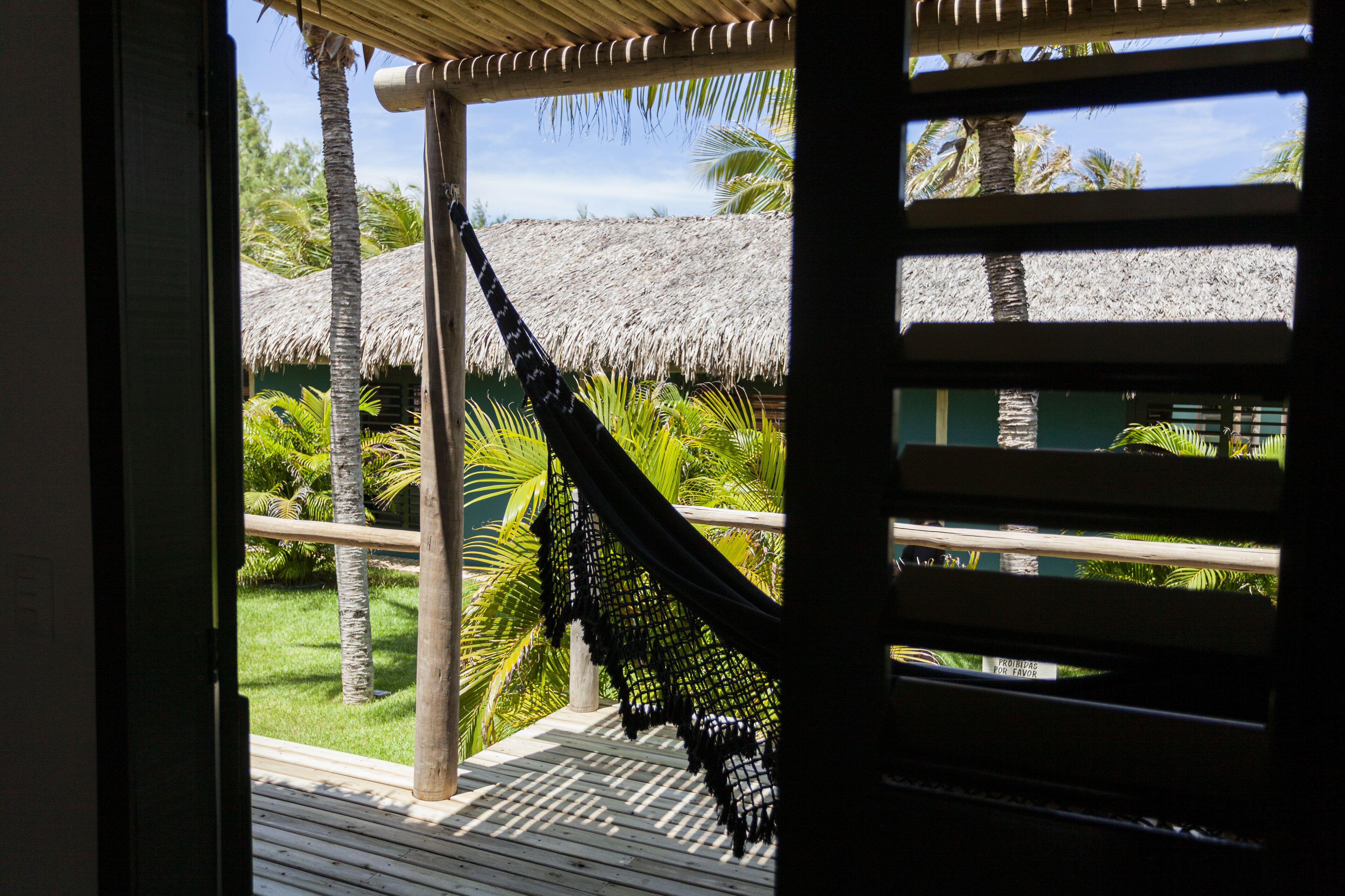 A wooden deck with a hammock, palm trees, and a thatched-roof structure.