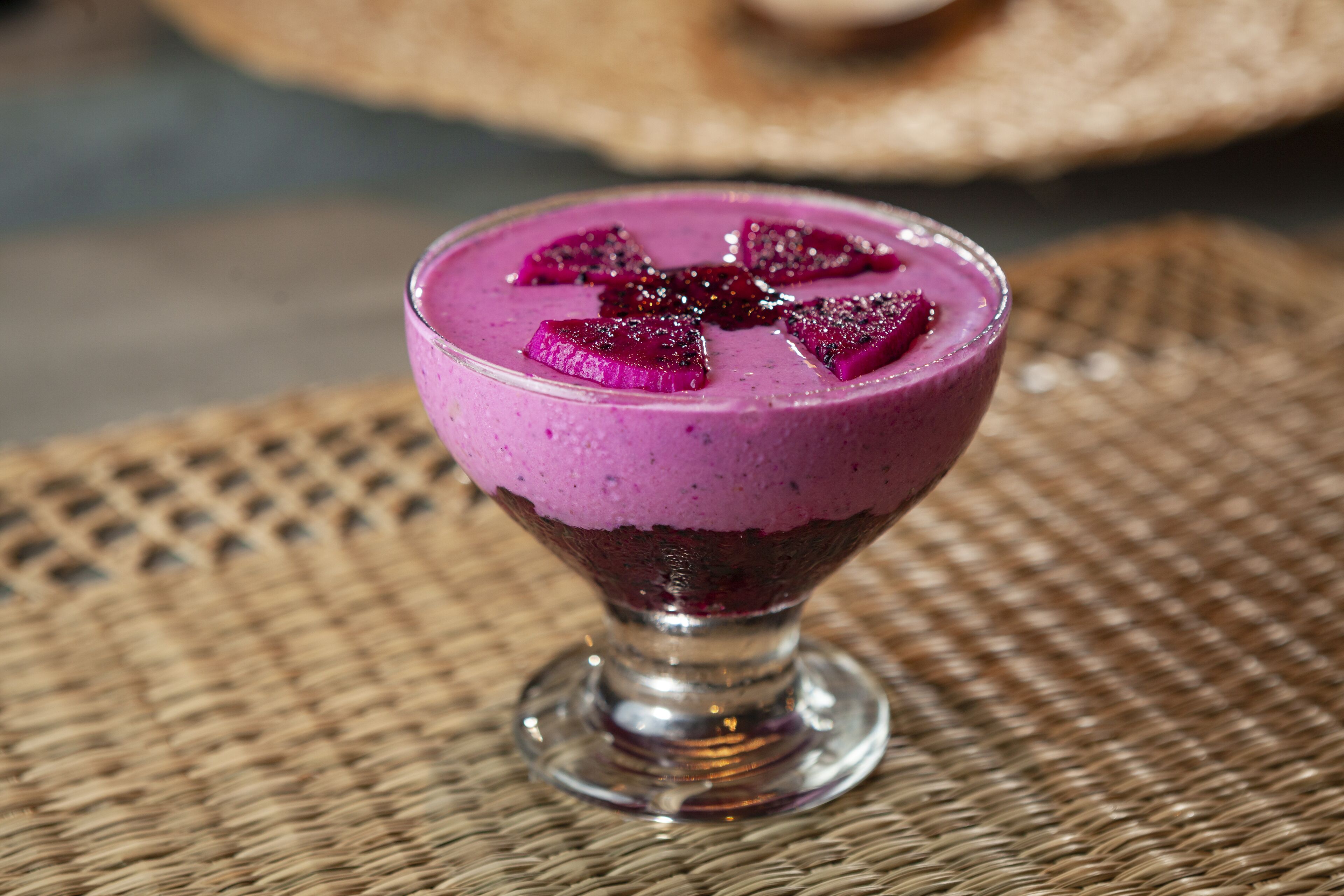 A purple smoothie in a glass on a woven mat.