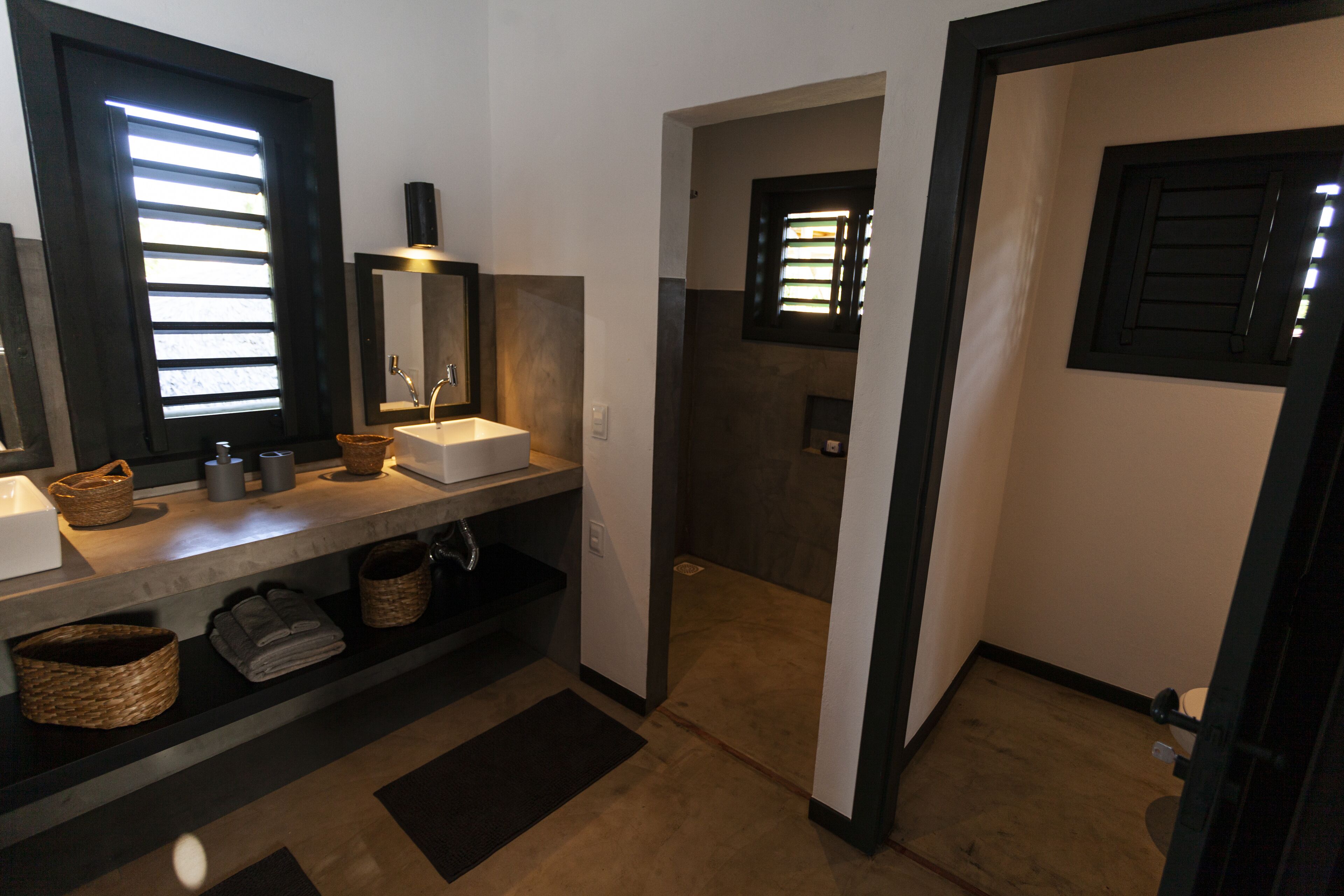 Ein Badezimmer mit zwei Waschbecken, einem Spiegel und einer Toilette. Auf der Ablage liegen Körbe und Handtücher.