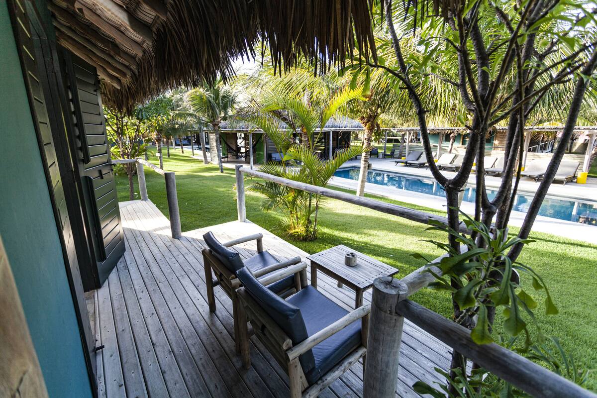 A wooden deck with a thatched roof, a pool, and lounge chairs.