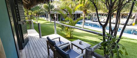 A wooden deck with a thatched roof, a pool, and lounge chairs.
