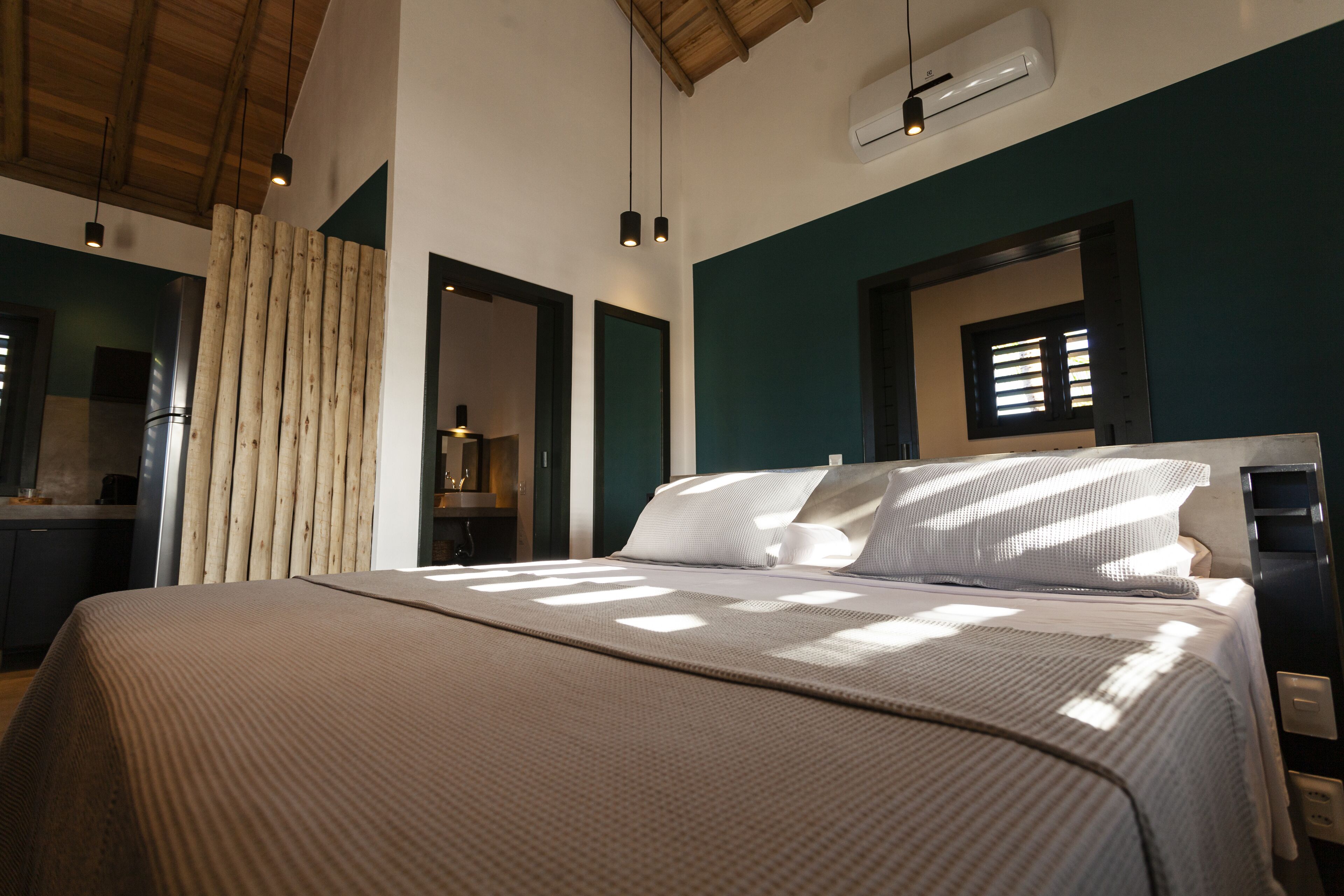 Ein modernes Hotelzimmer mit einem großen Bett, Holzlamellen und Blick zur Küche.