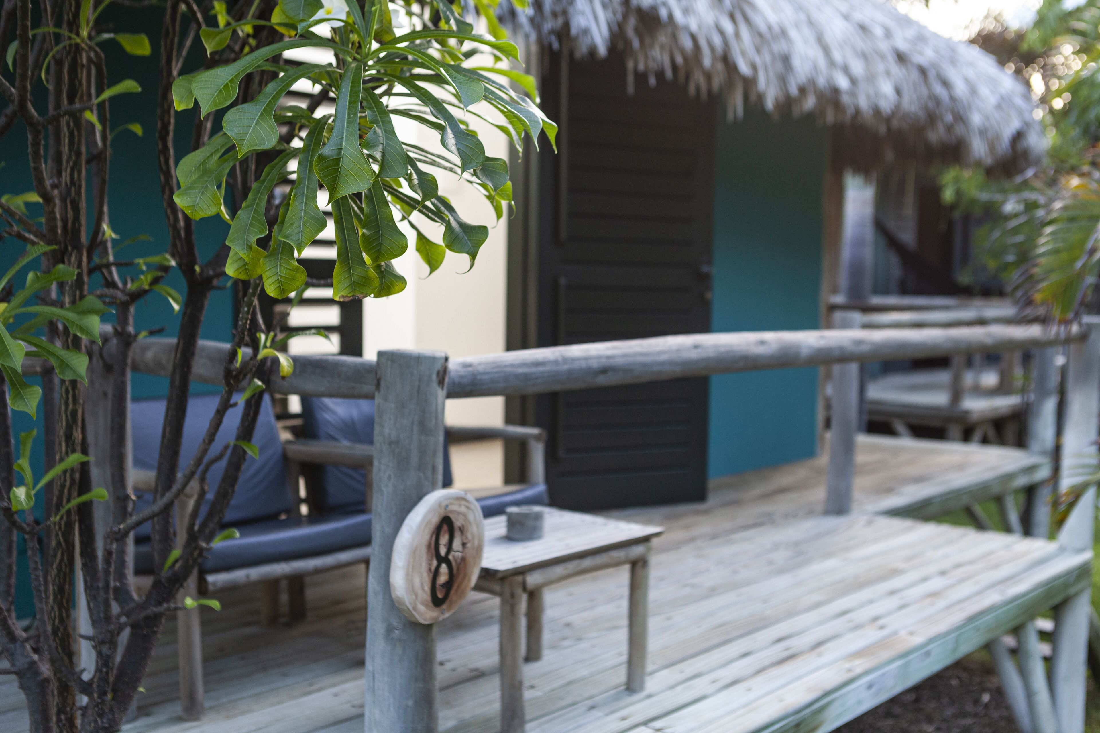 A wooden deck with a thatched-roof structure, a bench, and a table.