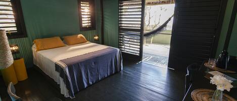 A room with a bed, a chair, a table with a vase of flowers, and a hammock outside.