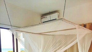 Een bed met een witte hemel en een plafondventilator, met uitzicht op zee.