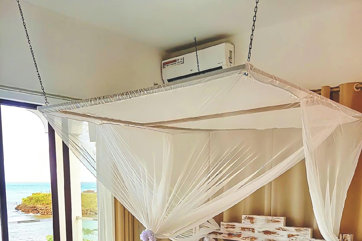 A bed with a white canopy, a view of the sea, and a ceiling fan.