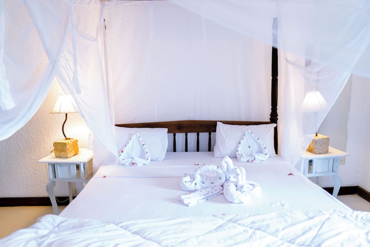 A neatly made bed with white linens, a wooden headboard, and a canopy. There are two bedside tables with lamps and a small decorative item on each.