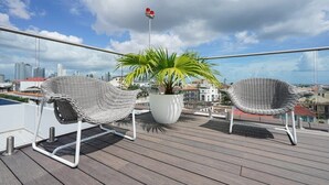A balcony with two wicker chairs, a potted plant, and a city view. - w* | Gorgeous 1BR in Casco Antiguo w/ Rooftop (Panamá)