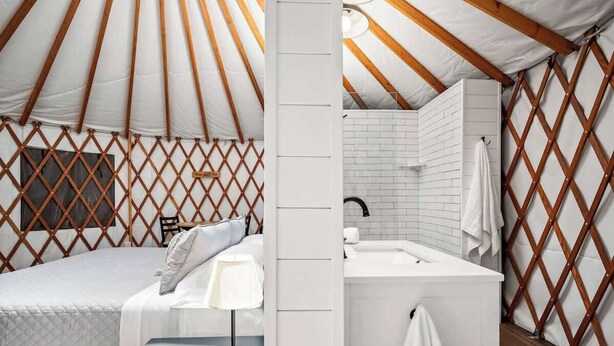 A yurt interior with a bed, a nightstand, a lamp, a white sink, and a wooden lattice wall. - OT 3515H Texas Yurt Haus Horned Frog (New Braunfels)
