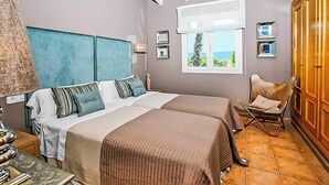 A bedroom with two beds, a window with a view, a wooden wardrobe, and a chair.