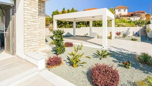 Patio moderno all'aperto con muro in pietra, zona relax coperta e aiuole fiorite.