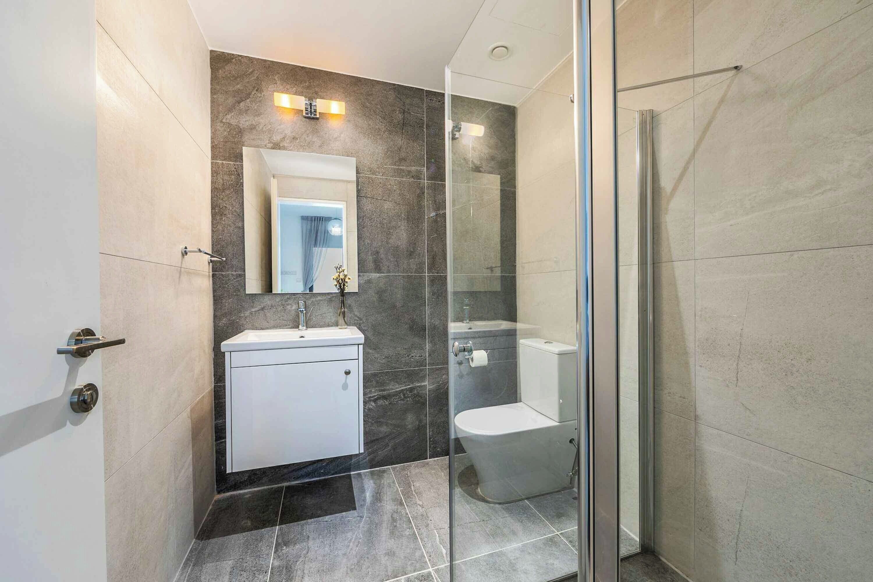A modern bathroom with a glass shower enclosure, a white sink, and a toilet.