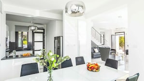 Una cucina moderna con isola centrale, un'area pranzo con tavolo e sedie bianche, e una scala che conduce a un piano superiore.