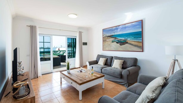 A living room with a grey sofa, a wooden coffee table, and a painting of a beach scene. - Villa Pargo - Three Bedroom Villa, Sleeps 6 (Playa Blanca)