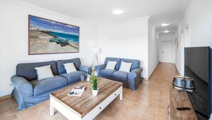 A living room with two grey sofas, a wooden coffee table, a painting of a beach, and a TV on the right. - Villa Pargo - Three Bedroom Villa, Sleeps 6 (Playa Blanca)