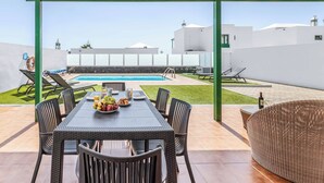 A covered outdoor dining area with a pool in the background. - Villa Bonaci - Three Bedroom Villa, Sleeps 6 (Playa Blanca)