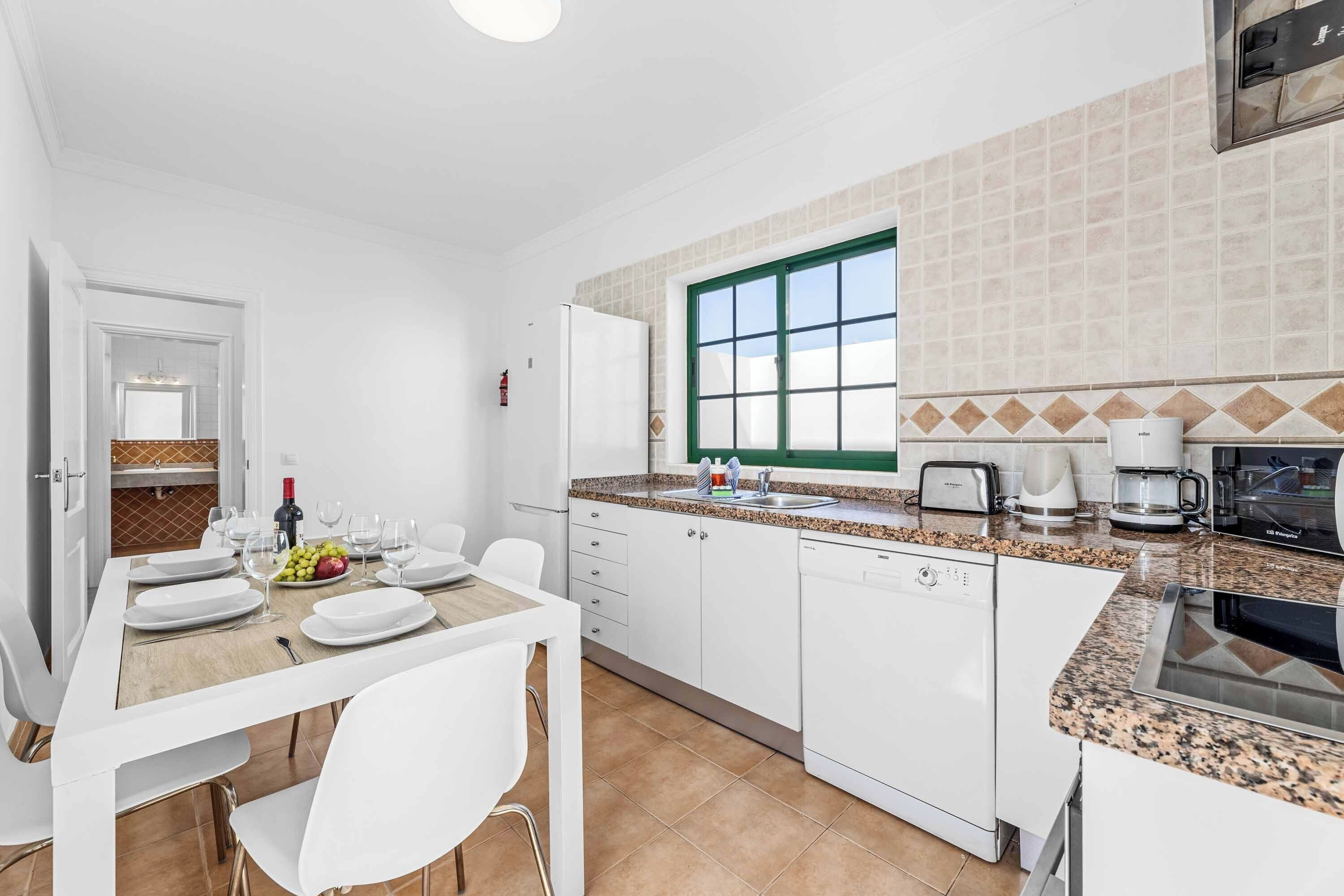 Una cocina moderna con armarios blancos, encimera de granito y ventana con marco verde.