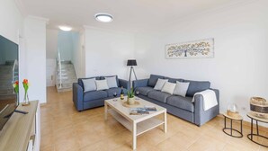 Een moderne woonkamer met een grijze bank, een houten salontafel en een trap op de achtergrond.