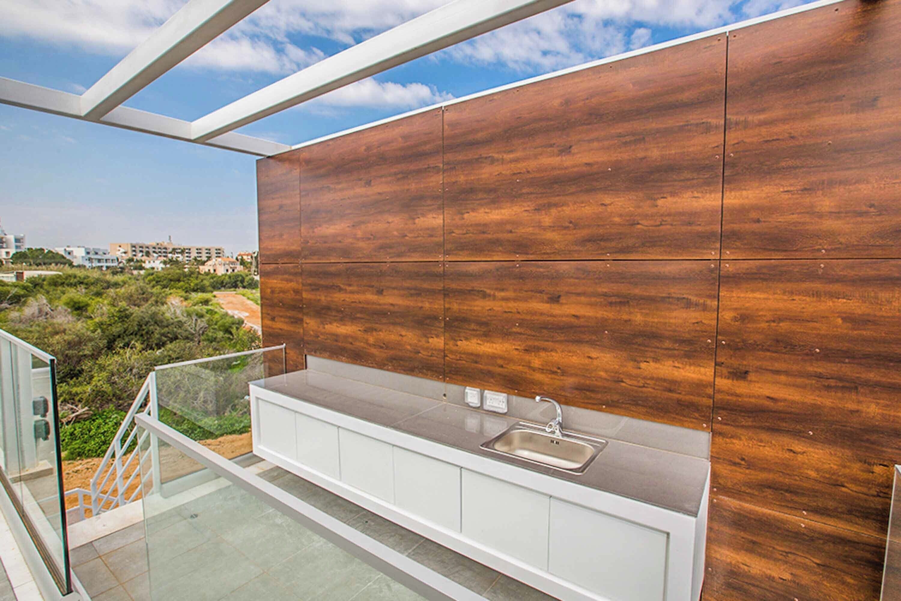 A modern kitchen with a wooden backsplash, a stainless steel sink, and a glass railing overlooking a scenic view.