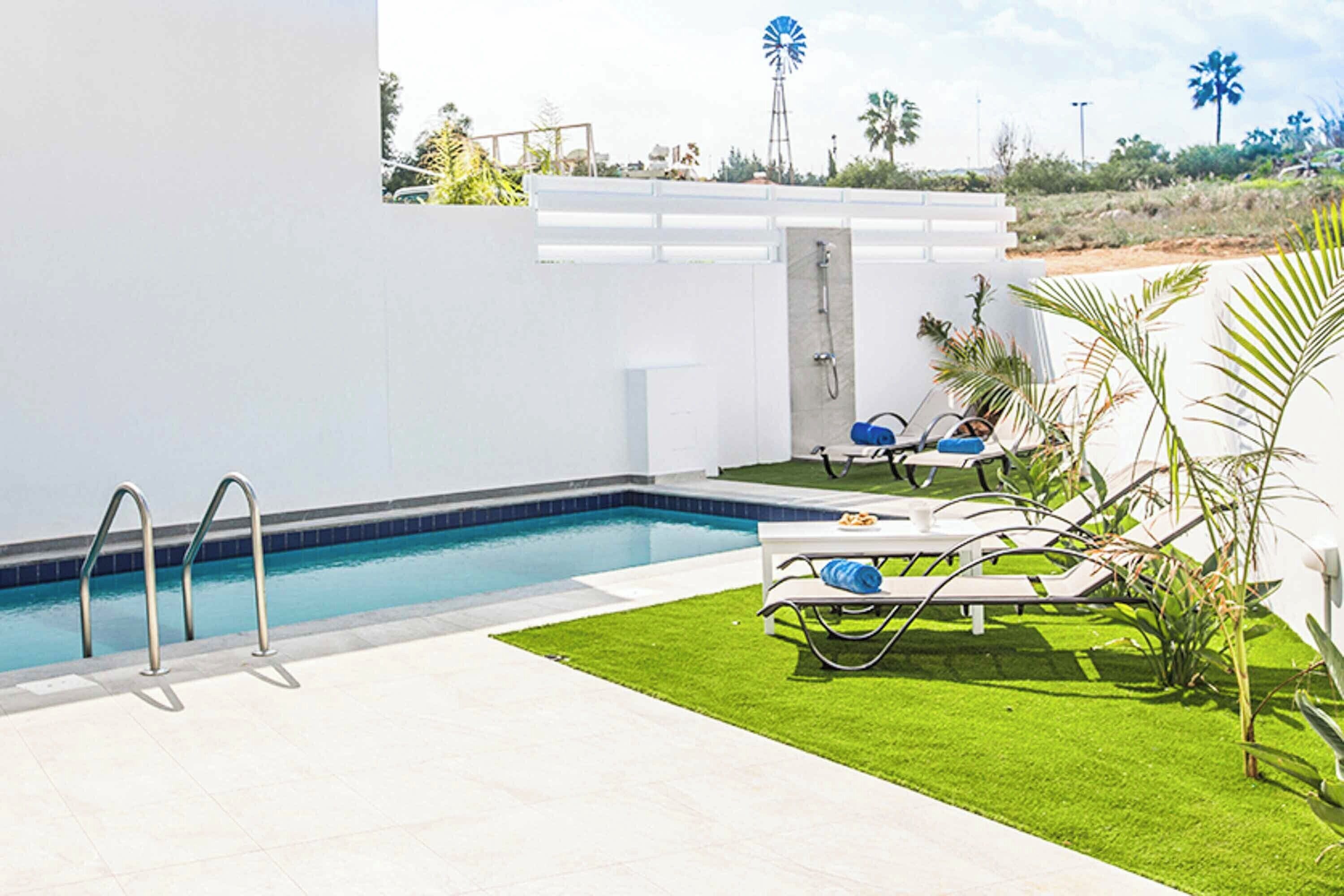 Un espace piscine avec un mur blanc, une porte et une petite table entourée de chaises.