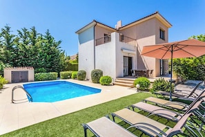 Une maison à deux étages avec une piscine, un patio doté de chaises longues et un espace extérieur aménagé avec des sièges.