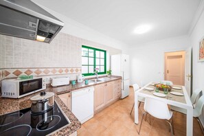 A compact kitchen with a microwave, stove, sink, and white cabinets.