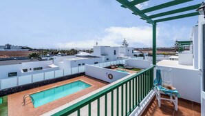 Un espace piscine aménagé sur le toit, offrant une vue dégagée sur le paysage environnant, un espace salon couvert et un bâtiment blanc doté d’une rambarde verte.
