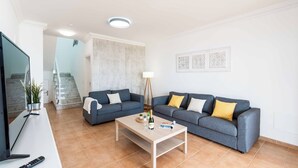 Un salon moderne avec deux canapés gris, une table basse, un téléviseur et un escalier en arrière-plan.